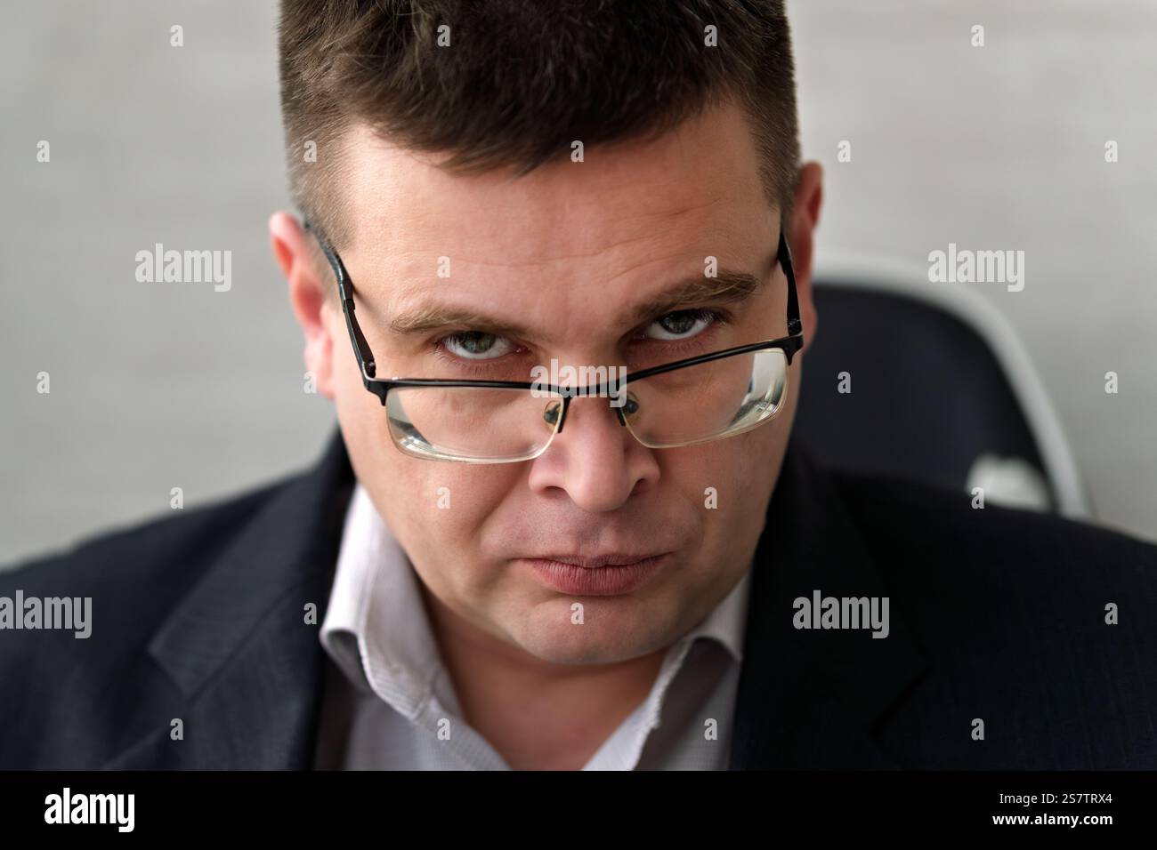 Stern Mittelalter Mann im Anzug, der über Brillen schaut. Ein Geschäftsmann in Brille mit ernsthaftem Blick schaut durchdringend in die Kamera. Stockfoto