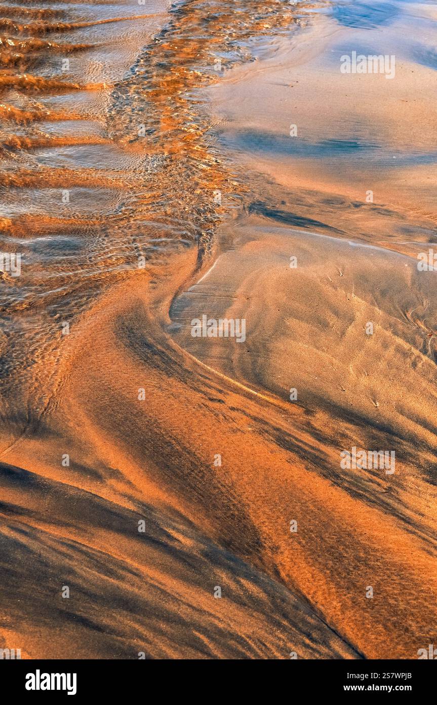 Das Bild zeigt die komplizierten Muster, die durch die Bewegung des Wassers über Sand entstehen. Das Wasser, reflektierendes Licht, hat den Sand geformt. Stockfoto