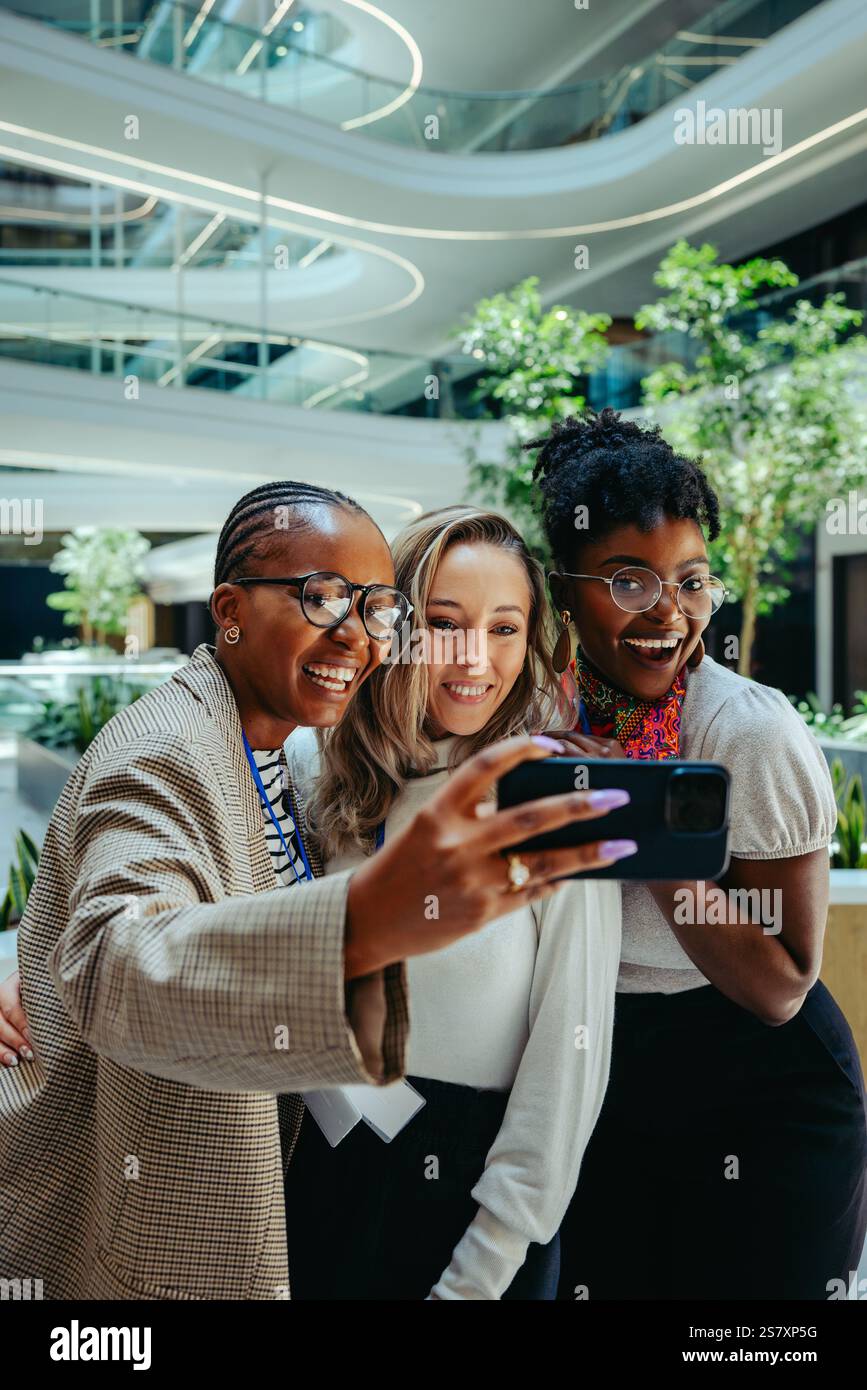 Drei verschiedene Kollegen machen ein Selfie in einer modernen Büroumgebung und halten einen Moment der Kameradschaft und Teamarbeit fest. Das stilvolle Ambiente mit Grün Stockfoto