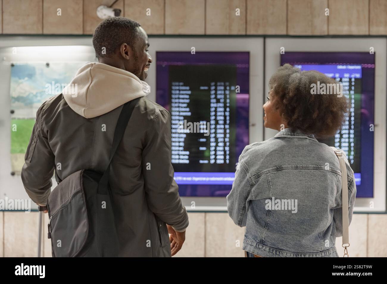 Afroamerikanisches Paar überprüft den Fahrplan Ankunft Abfahrtskarte an einem Bahnhof. Informations-, Transport- und Tourismuskonzepte. Stockfoto