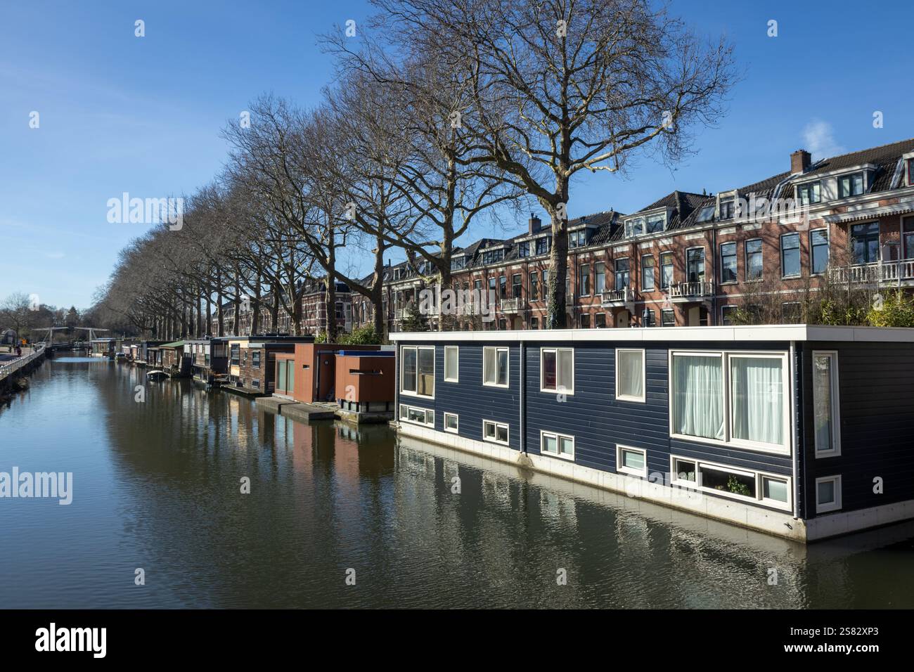 Hausboote in Utrecht an einem sonnigen Tag mit blauem Himmel und Bäumen und Backsteinhäusern im Hintergrund, Brücke Stockfoto