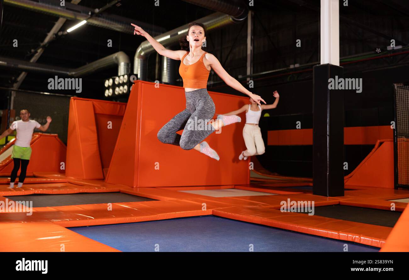 Glückliche Frau mittleren Alters, die auf Trampolinen in einem Sporthalle trampoliniert und springt, Workout und modernes Unterhaltungskonzept Stockfoto