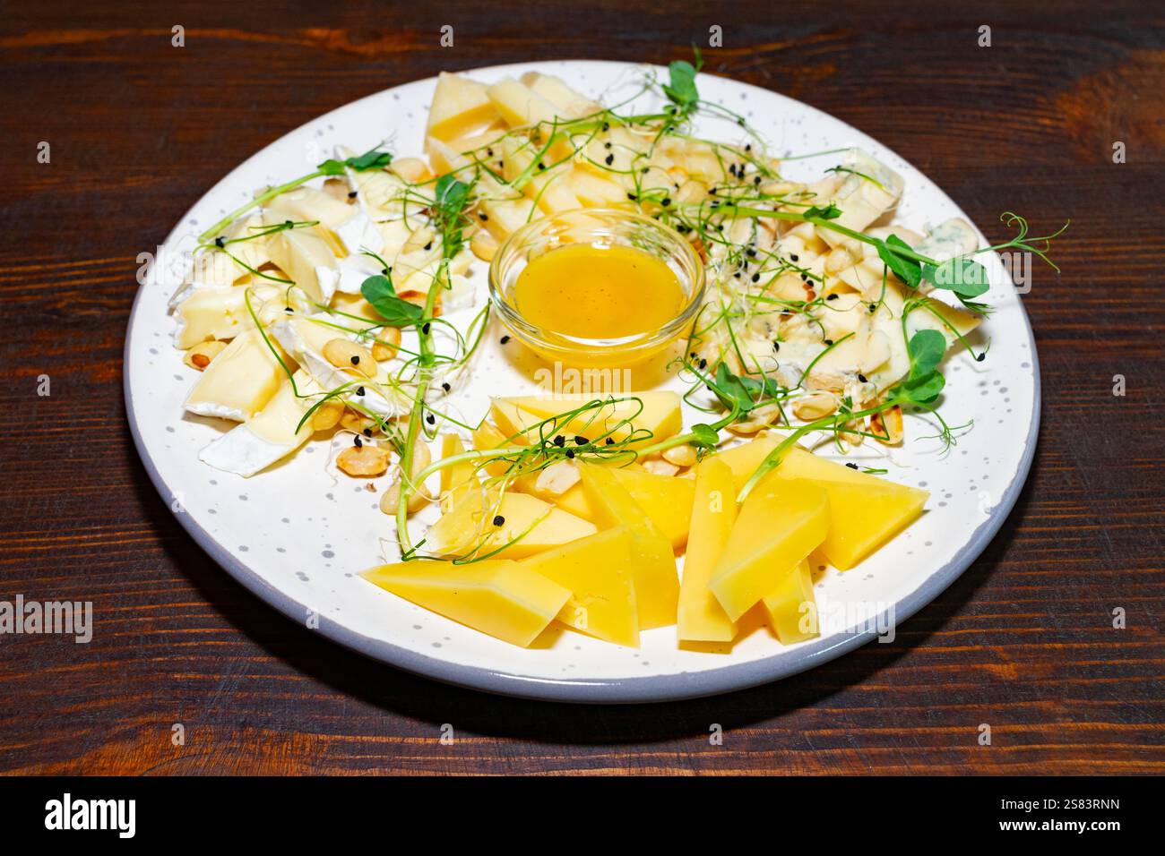 Eine Gourmet-Käseplatte wird auf einem rustikalen Holztisch präsentiert. Die Auswahl umfasst verschiedene Käsesorten, begleitet von Honig und garniert mit fr Stockfoto