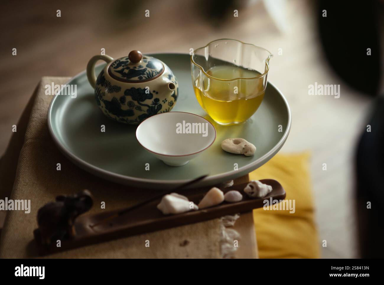 Stillleben Foto von gemusterter Teekanne aus Ton, klarem Glaskrug, Teetasse mit frisch gebrühtem Oolong-Tee auf Tablett im Zeremoniezimmer. Weiches Licht, Holztee Stockfoto