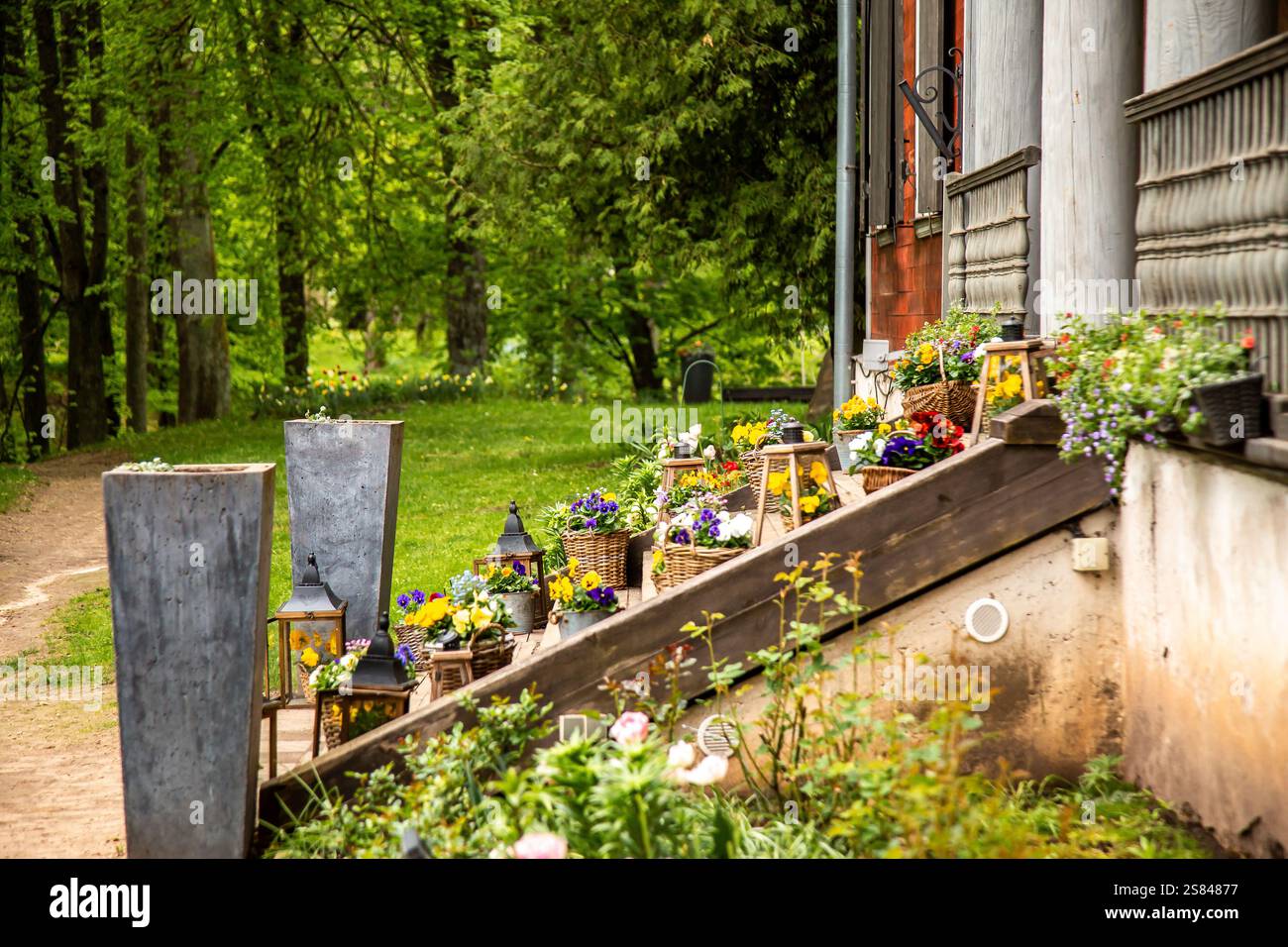 Rustikale Holztreppe mit bunten Topfblumen und Laternen, die zu einem verwitterten Gebäude mit Holzverkleidungen und roten Backsteinakzenten führt. Stockfoto