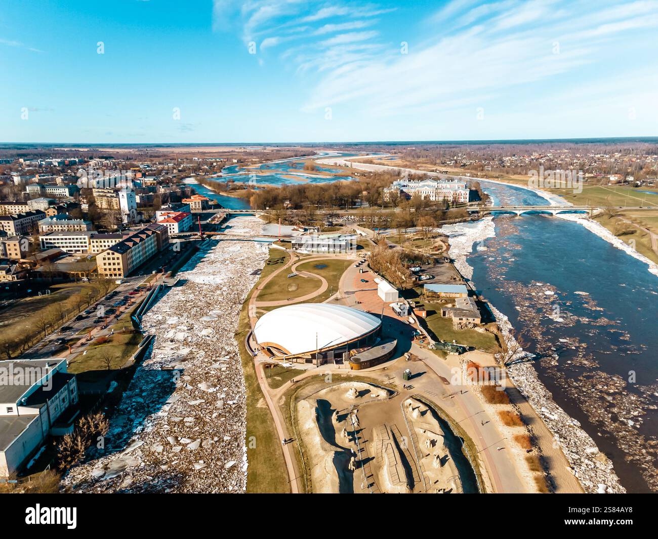 Aus der Vogelperspektive einer Stadt an einem teilweise gefrorenen Fluss mit Eisschollen, mit einer weißen Kuppelstruktur, einer Brücke und einer Mischung aus modernem und historischem Stockfoto
