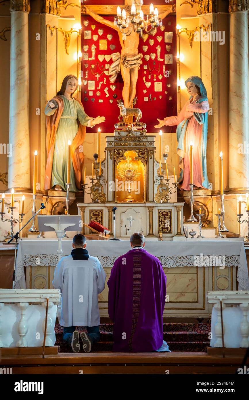 Ein religiöser Altar in einer Kirche mit einem Kruzifix, einer Marienstatue, goldenen Akzenten, Kerzen und Geistlichen, die im Gebet knieten. Stockfoto