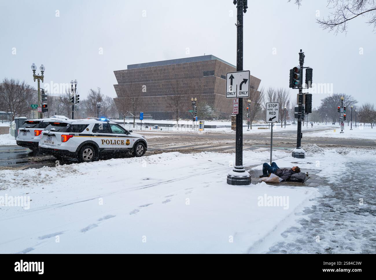 Ein Mann wärmt sich auf einem Heizungsfall, während zwei Polizeiautos während eines Schneesturms an der 15th Avenue NW in der Nähe des Weißen Hauses vorbeifahren. Stockfoto