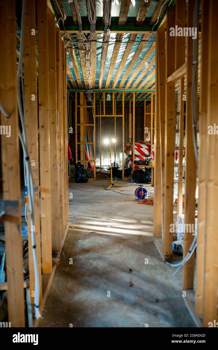 Freiliegende Holzrahmen, Elektrokabel und Dämmung in einem Gebäude im Bau. Werkzeuge und Materialien sind über die unfertige Fläche verstreut Stockfoto