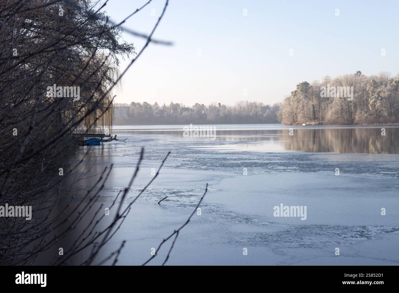 Eine heitere Winterszene in Straussee mit teilweise gefrorenem Wasser, das die frostbedeckten Bäume unter klarem blauem Himmel reflektiert. Stockfoto