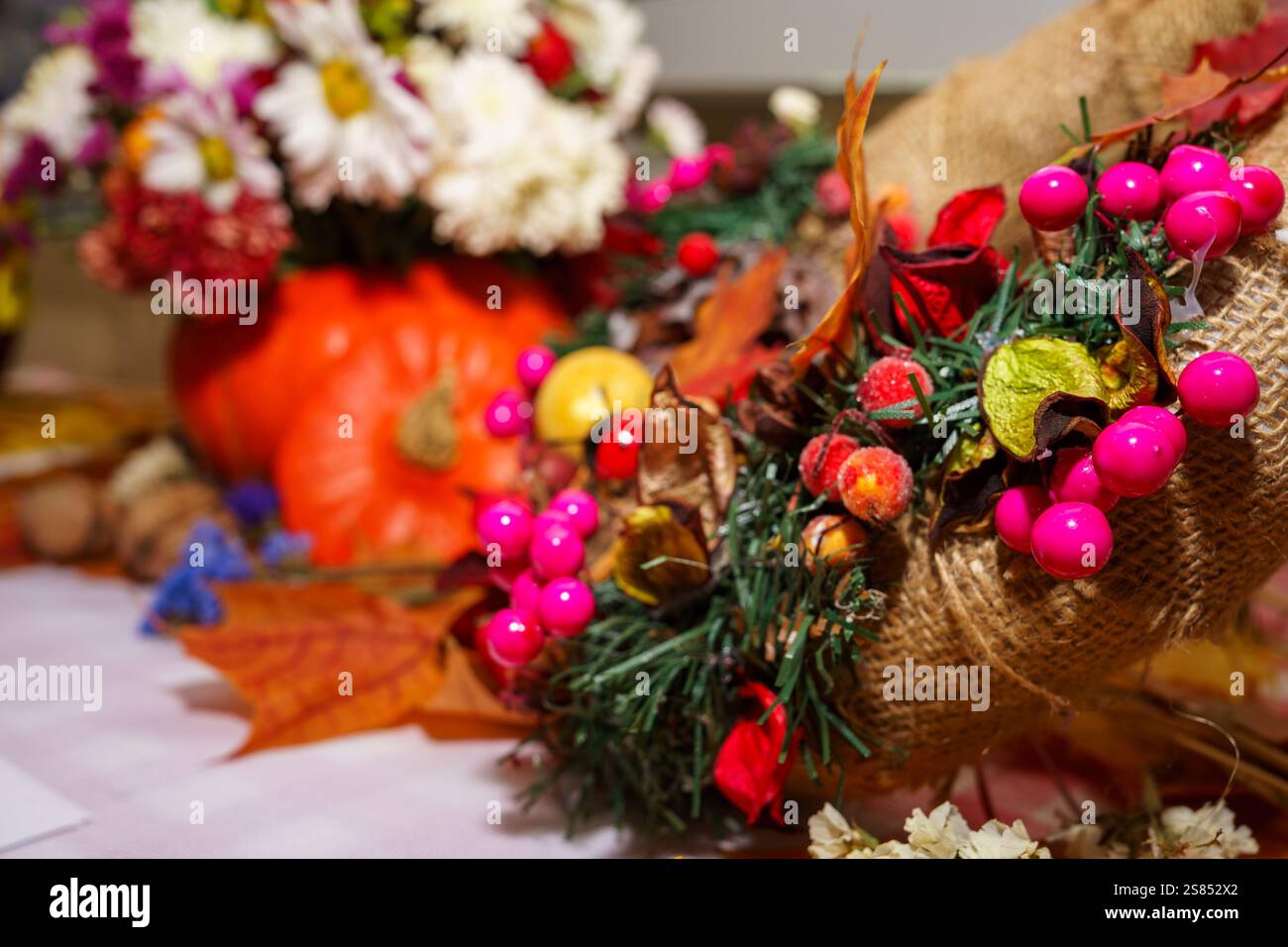 Leuchtend rosa Beeren und getrocknete Blätter bilden den Mittelpunkt des Herbstes. Ein Kürbis sorgt für Wärme, während Blumen im Hintergrund die festliche Atmosphäre verbessern Stockfoto