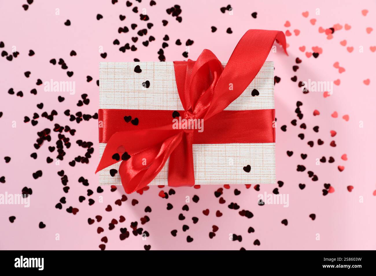 Romantisches Geschenk und Konfetti auf hellrosa Hintergrund, Draufsicht Stockfoto