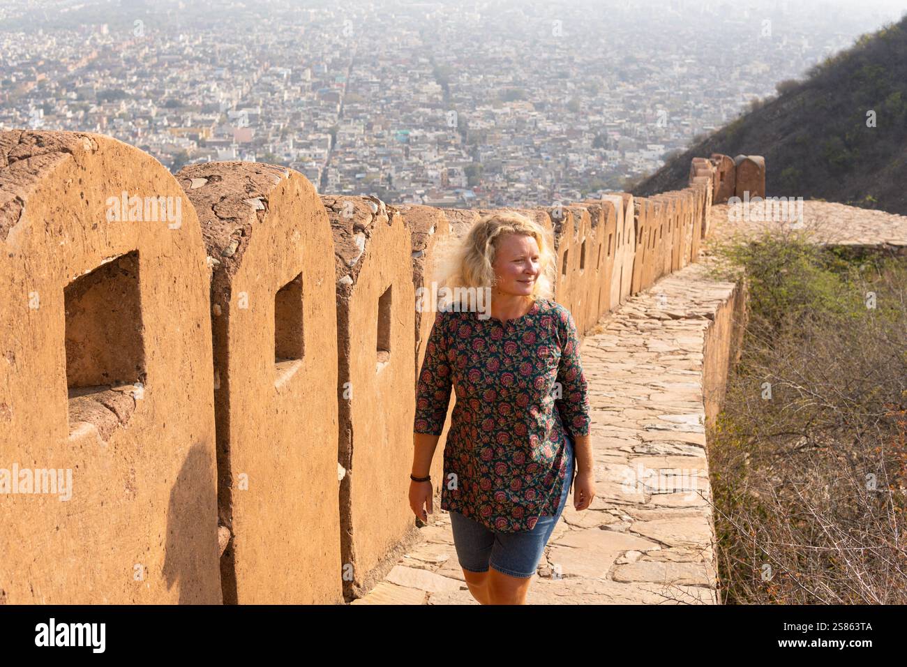 Junge blonde Frau, die an heißen sonnigen Tagen in Rajasthan, Indien, an den Wänden der rosa Stadt Jaipur spaziert. Stockfoto