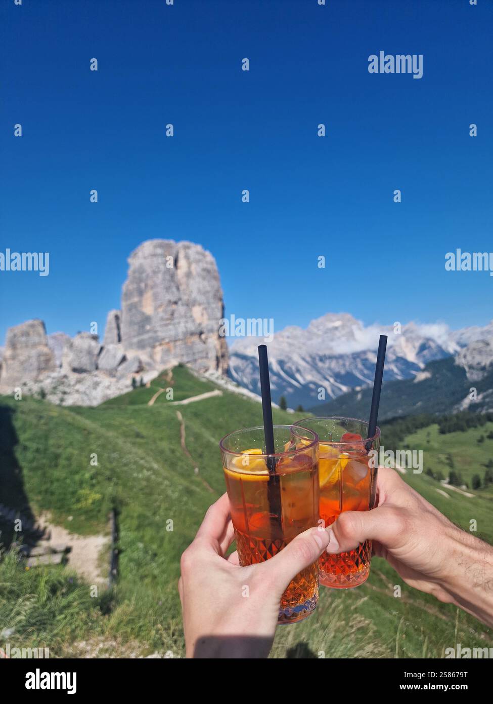 Hände halten erfrischende Getränke vor dem klaren blauen Himmel in den Bergen. Zwei Freunde jubeln mit Gläsern erfrischender aperol Spritz Drinks Stockfoto