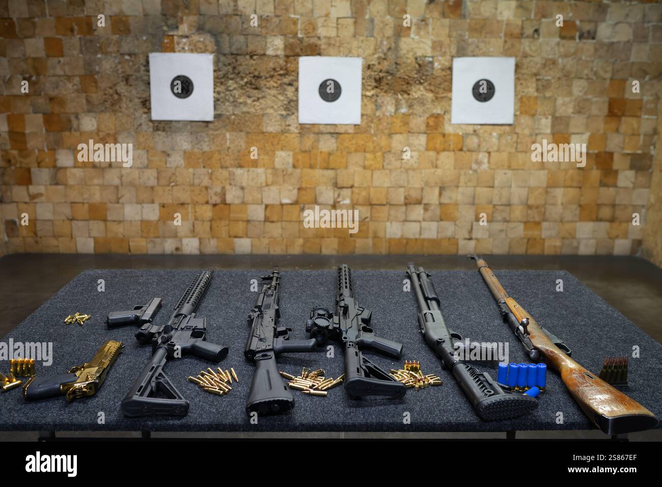 Verschiedene Schusswaffen auf einem Tisch in einem Schießstand, Papierziele hängen an der Wand einer Schussfalle. Stockfoto