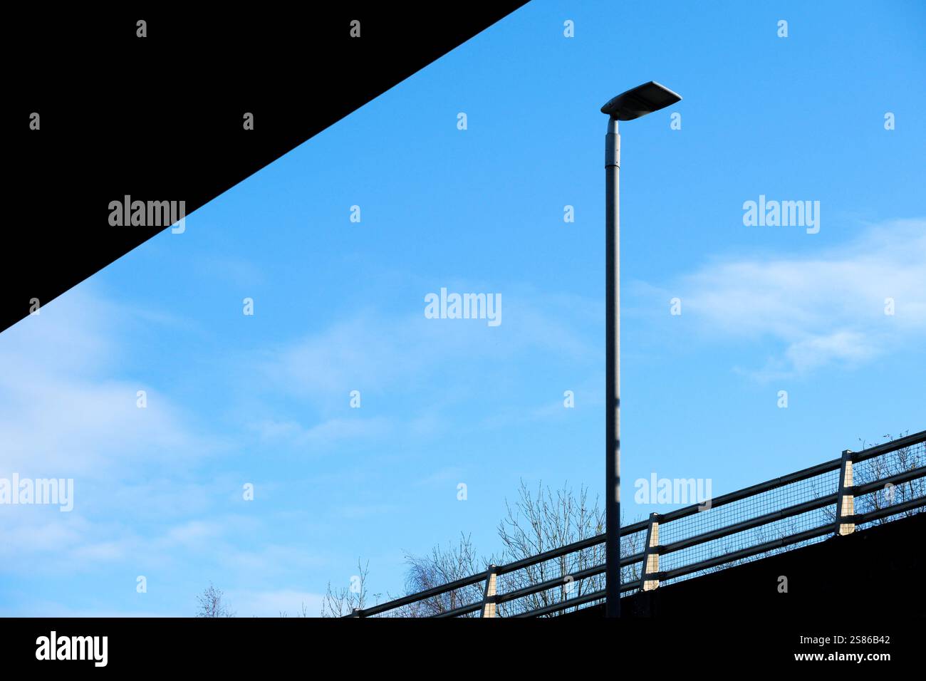 Detail einer Beton- und Stahlbrücke über eine Autobahn mit blauem Himmel und einem Leuchtenpfosten. Stockfoto