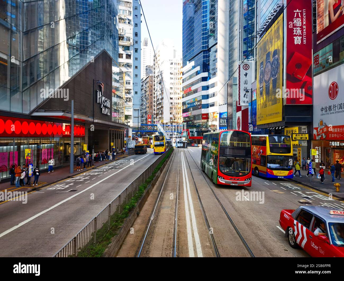 Hongkong, China - 21. Januar 2025 : Eine belebte Straßenszene, von einer Straßenbahn aus gesehen, zeigt hochaufragende Wolkenkratzer, lebhafte Werbung und Busse Stockfoto