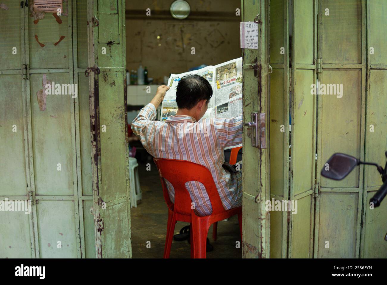 GEORGE TOWN, MALAYSIA - 24. JANUAR 2024: Chinese liest eine Zeitung in einem der Häuser auf traditionellen Clan-Anlegestellen auf Penang Island Stockfoto