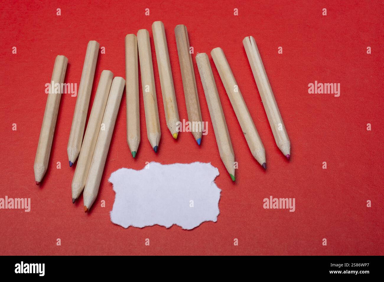 Buntstifte auf rotem Hintergrund und zerrissenes Papier Stockfoto