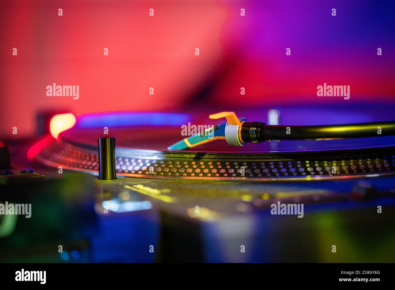 Plattenspieler mit Schallplattendetails bei schlechten Lichtverhältnissen. Schallplatte auf rotem und blauem Hintergrund des Drehsockels. Details der Drehsockelnadel sind dokumentiert. Stockfoto