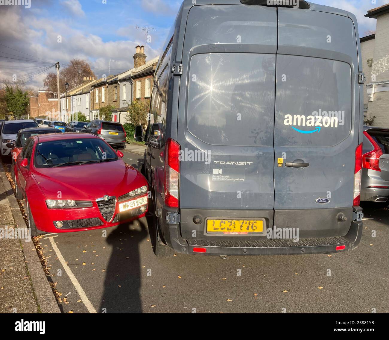 Ein schlecht gefahrener Amazon Lieferwagen kommt beim Absetzen eines geparkten Fahrzeugs sehr nahe, was auf ein schlechtes Manöver des Fahrers beim Einbiegen in die Straße zurückzuführen ist. Die Nummernschilder des Fahrzeugs sind verpixelt. UK (138) Stockfoto