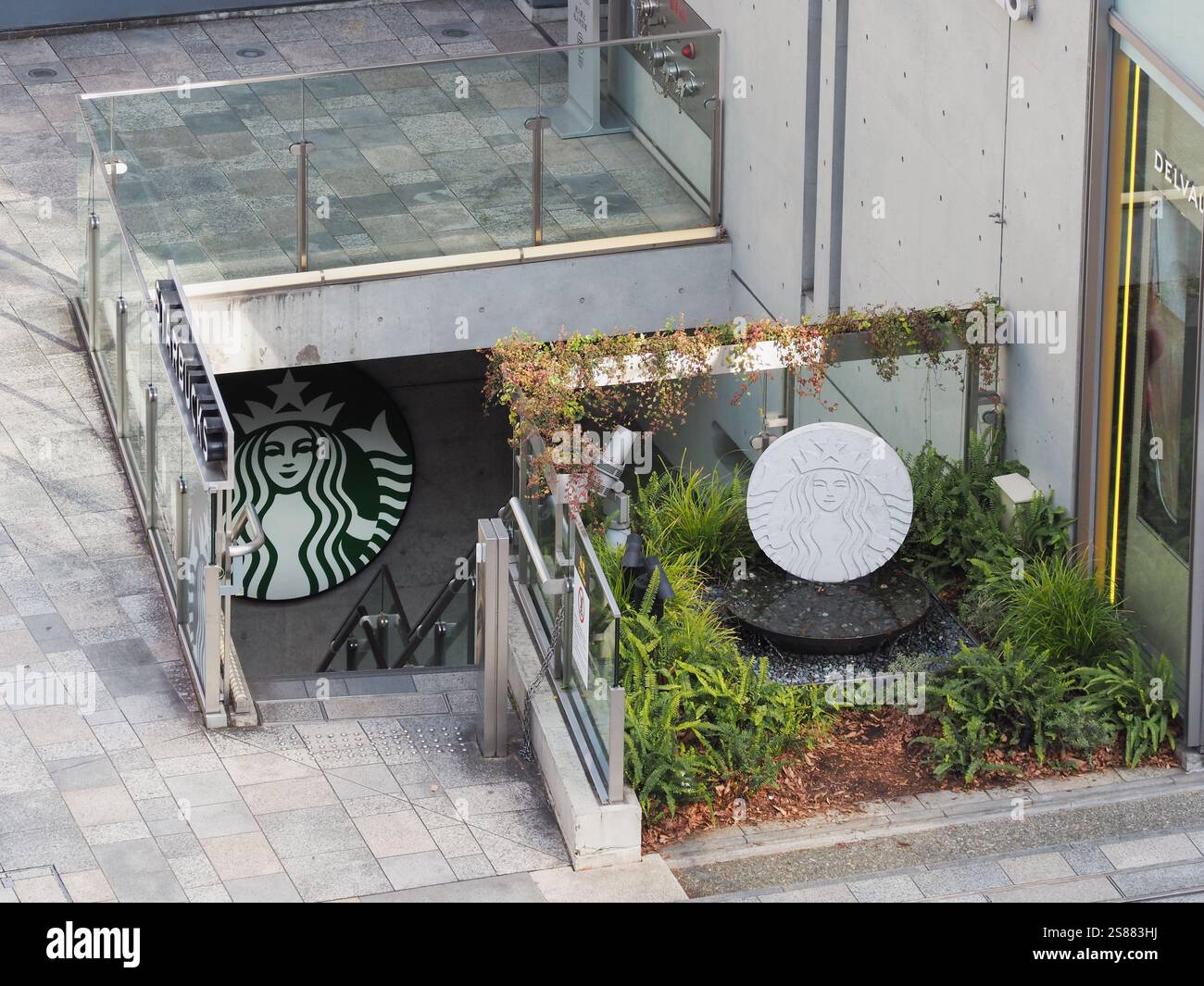 Rand des Einkaufskomplexes Omotesando Hills in Tokio mit einem Starbucks-Symbol und Brunnen mit Stufen, die zu einem Café im Untergeschoss führen. Stockfoto
