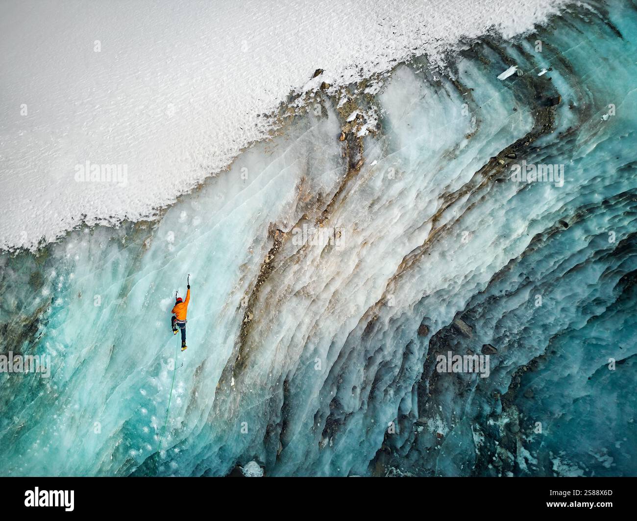 Luftaufnahme eines Athleten in orangefarbener Jacke Eisklettern an der großen gefrorenen Eiswand des Bogdanovich-Gletschers im Bergtal in Kasachstan Stockfoto