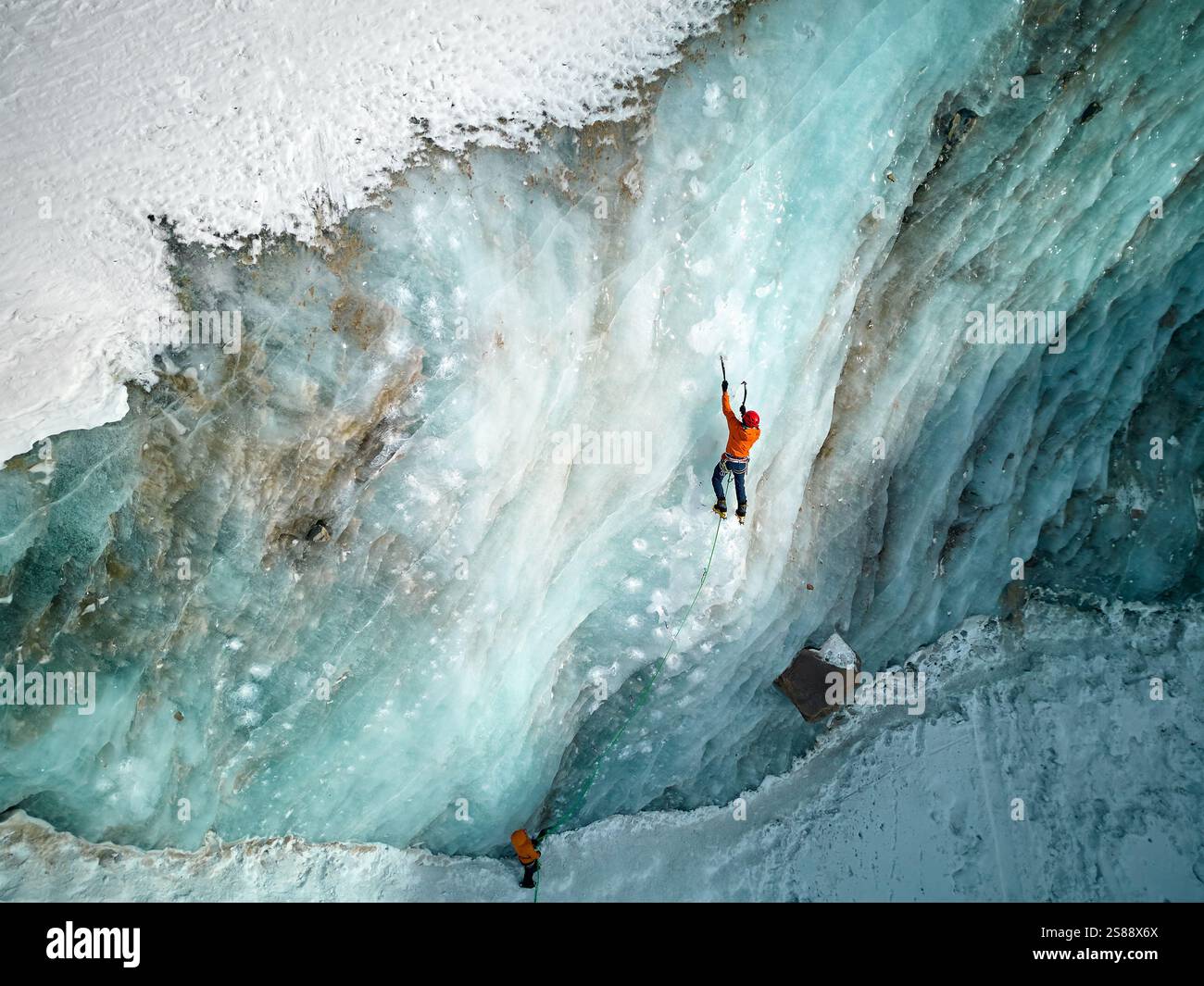 Luftaufnahme eines Athleten in orangefarbener Jacke Eisklettern an der großen gefrorenen Eiswand des Bogdanovich-Gletschers im Bergtal in Kasachstan Stockfoto