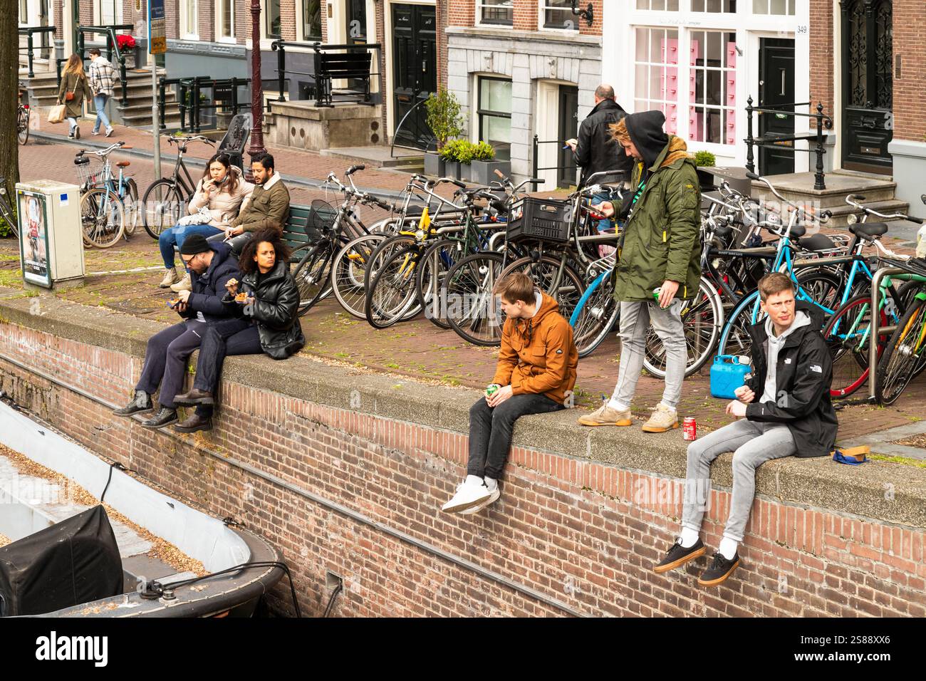 Touristen mit einem Snack und einer Dose auf der Kaimauer der Keizersgracht in Amsterdam. Stockfoto