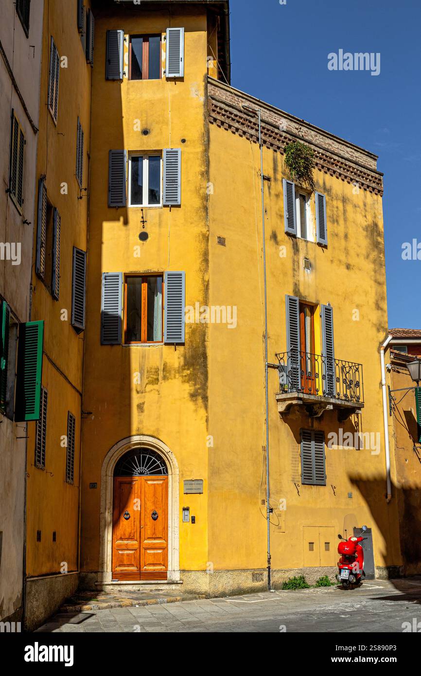 Ein Vespa-Roller parkte vor einem gelben Gebäude mit Holzläden in der mittelalterlichen Stadt Siena, Italien Stockfoto