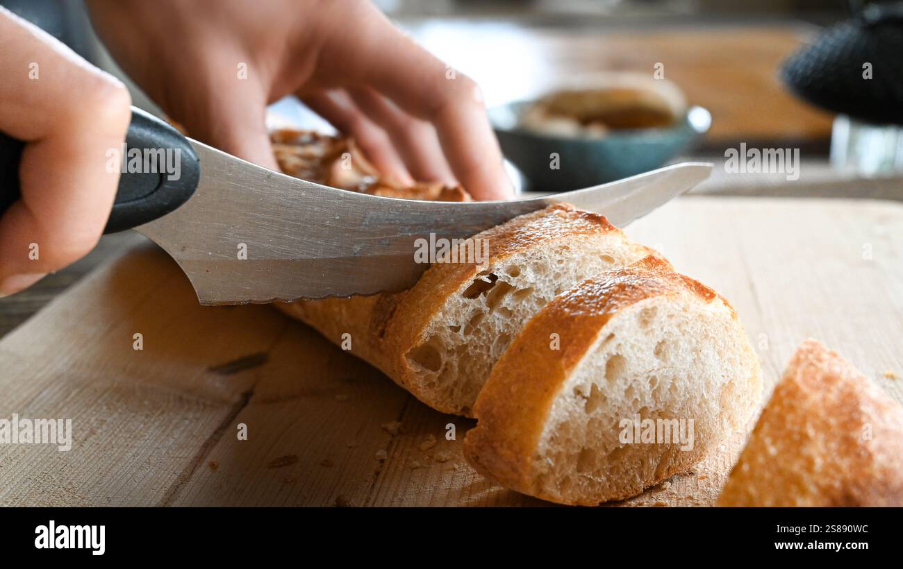 Frisches Baguette wird zum Frühstück in Scheiben geschnitten. Brot schneiden. Holzbrett mit Messer und Brot. Stockfoto