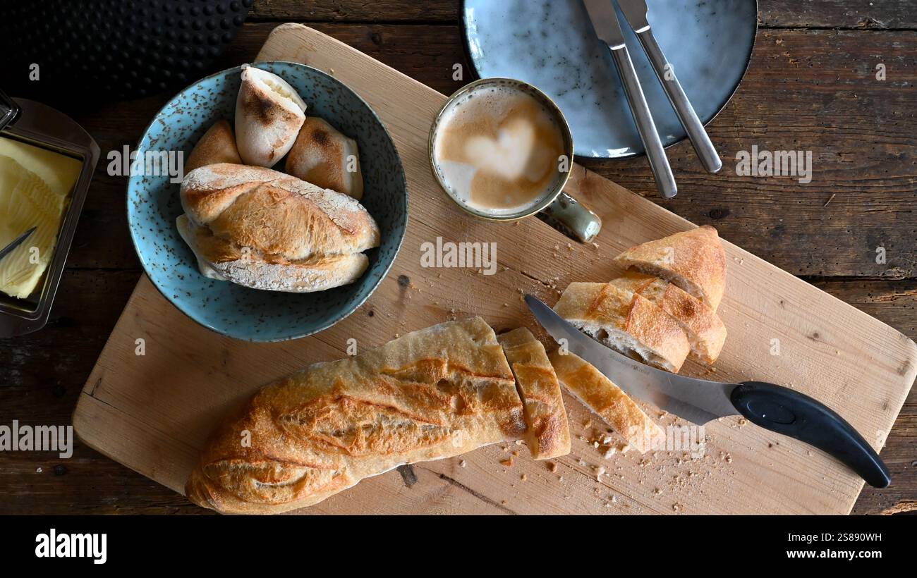 Frisches Baguette wird zum Frühstück in Scheiben geschnitten. Brot schneiden. Holzbrett mit Messer und Brot. Stockfoto