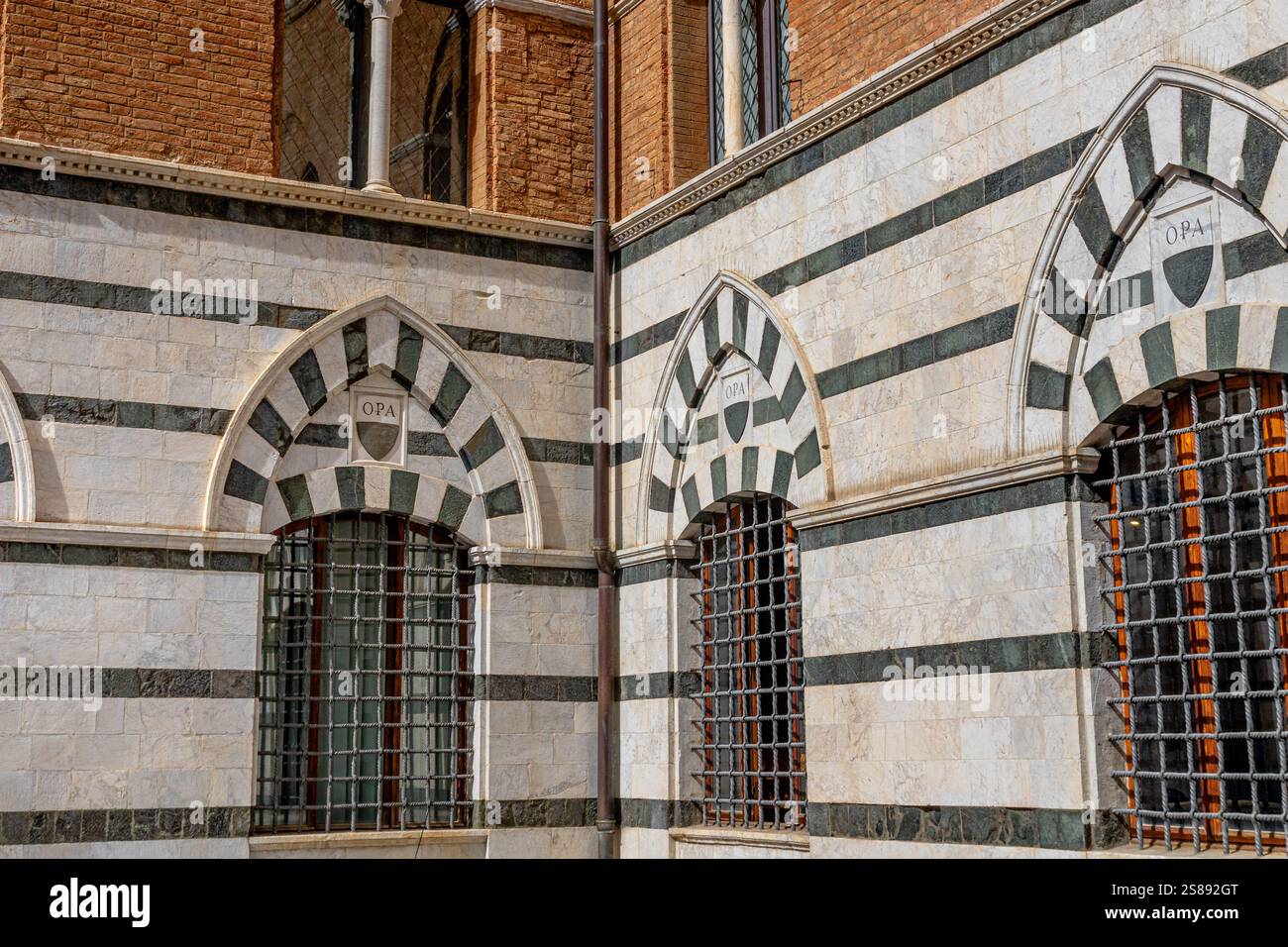 Dekorative mittelalterliche Bogenfenster mit Metallstangen in einem Gebäude an der Piazza del Duomo, Siena, Italien Stockfoto