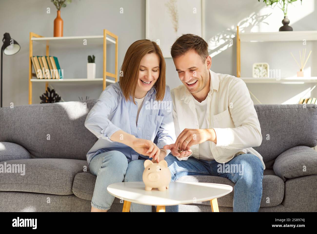 Glückliches, junges Paar, das auf dem Sofa sitzt, Geld in der Sparkasse spart und zu Hause über Finanzpläne diskutiert. Stockfoto