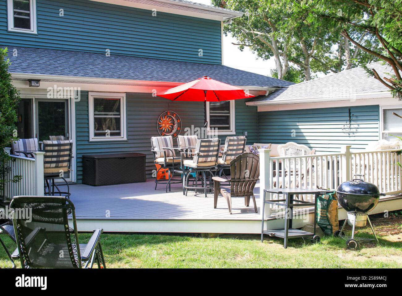 Helle Terrasse mit Sitzgelegenheiten und rotem Sonnenschirm ist perfekt für Familienfeiern im Sommer. Stockfoto
