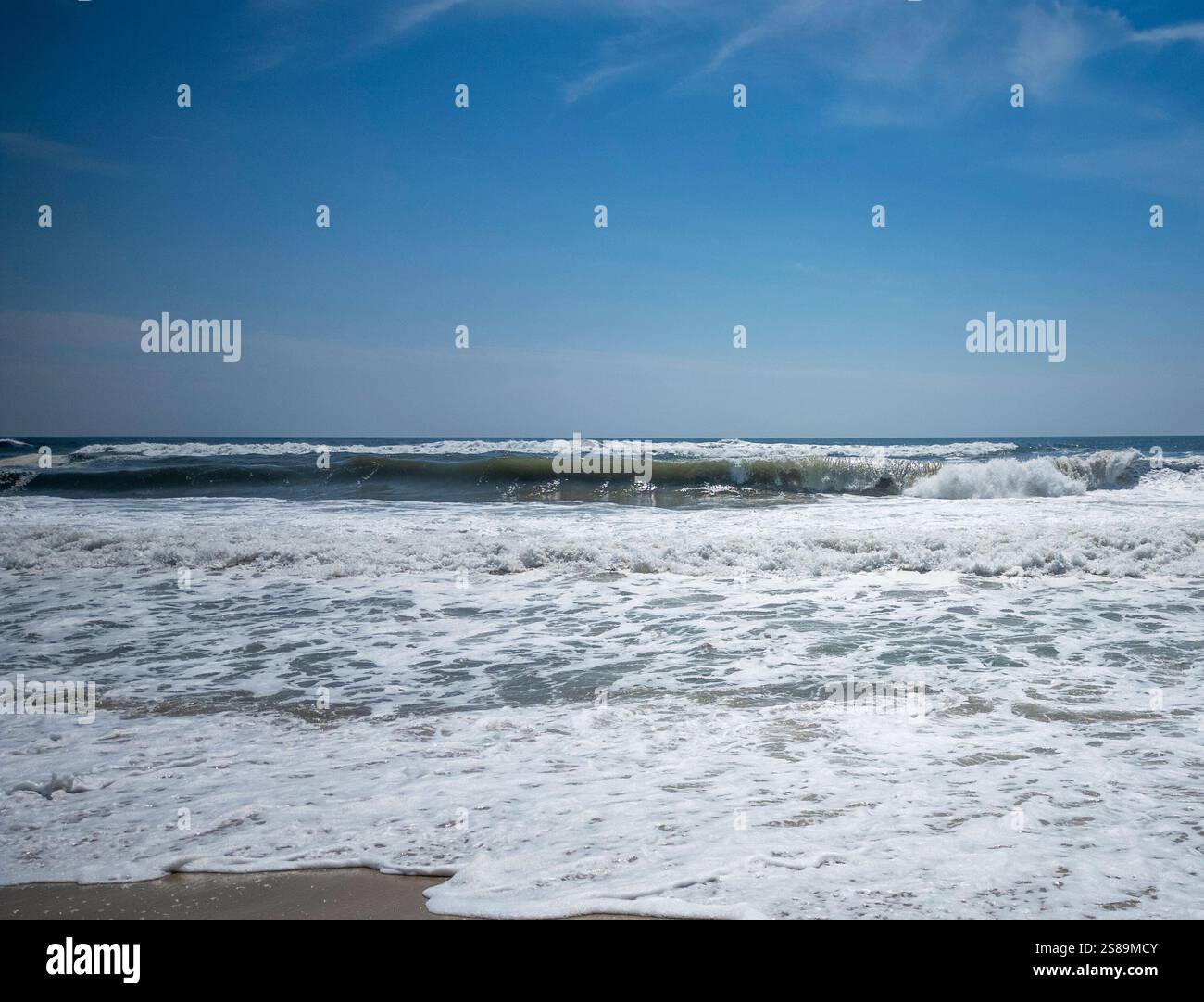 Wunderschöne Wellen Rollen auf den Sandstrand, während das Sonnenlicht den Himmel und das Wasser am Nachmittag erhellt. Stockfoto