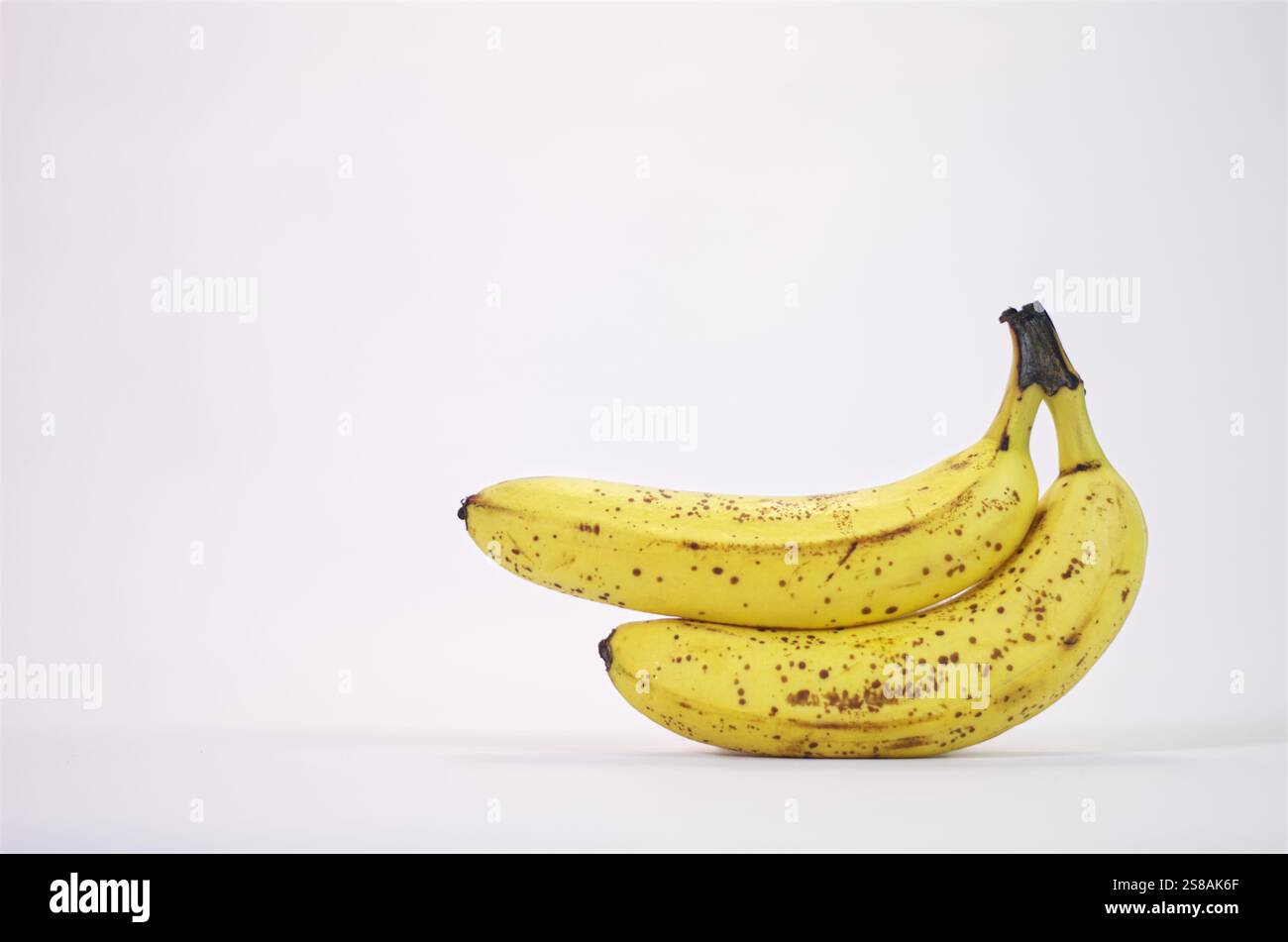 Frische reife Bananen mit gepunkteten Häuten, die natürliche Früchte und gesunde Ernährung auf weißem Hintergrund symbolisieren und eine einfache und saubere Zusammensetzung schaffen. Stockfoto