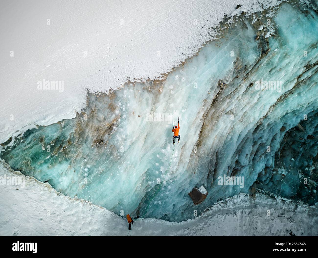 Luftaufnahme eines Athleten in orangefarbener Jacke Eisklettern an der großen gefrorenen Eiswand des Bogdanovich-Gletschers im Bergtal in Kasachstan Stockfoto