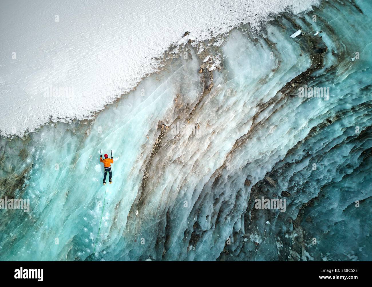 Luftaufnahme eines Athleten in orangefarbener Jacke Eisklettern an der großen gefrorenen Eiswand des Bogdanovich-Gletschers im Bergtal in Kasachstan Stockfoto