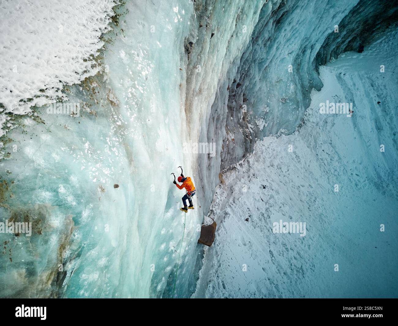 Luftaufnahme eines Athleten in orangefarbener Jacke Eisklettern an der großen gefrorenen Eiswand des Bogdanovich-Gletschers im Bergtal in Kasachstan Stockfoto