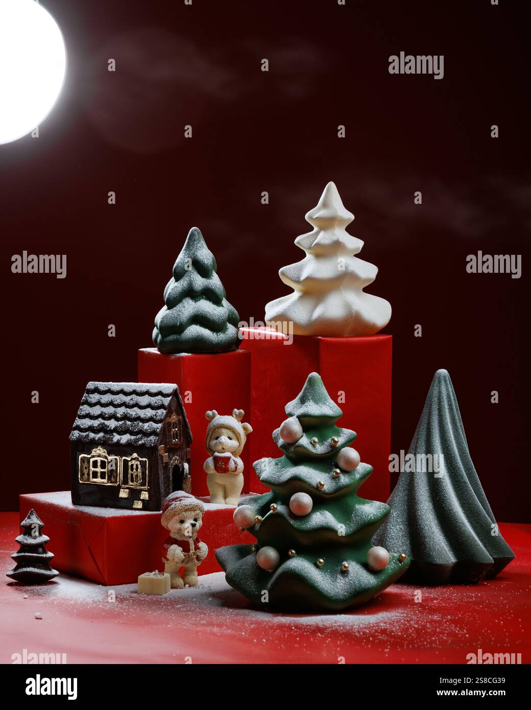 Weihnachtshintergrund mit Geschenkboxen und farbenfrohen Schokoladenfiguren von Weihnachtsbäumen, Bären, Kugeln. Roter Hintergrund Stockfoto