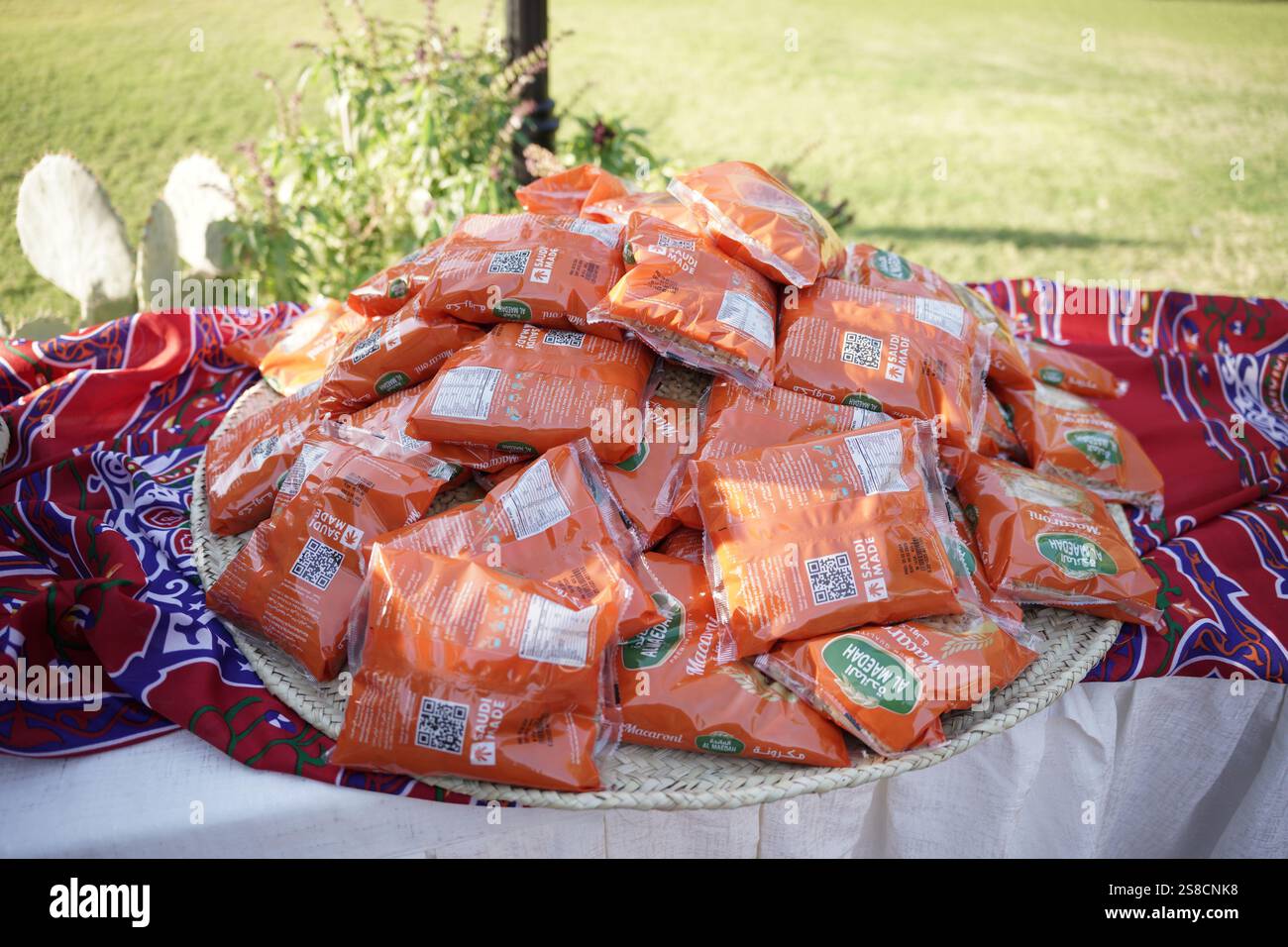 Ein gewebter Korb gefüllt mit orangen Makkaroni, wunderschön auf lebendigem arabischem Stoff im Ramadan-Stil. Eine perfekte Ergänzung zum Ramadan-Essen Stockfoto