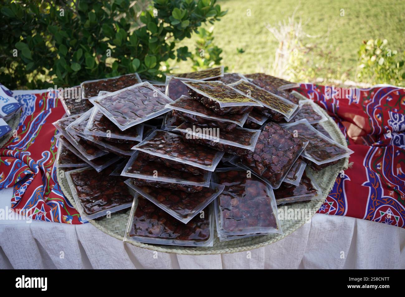 Ein gewebter Korb gefüllt mit vakuumverpackten Datteln auf einem farbenfrohen Stoff im Ramadan-Stil. Das Display zeigt eine perfekte Balance aus Tradition und Komfort Stockfoto