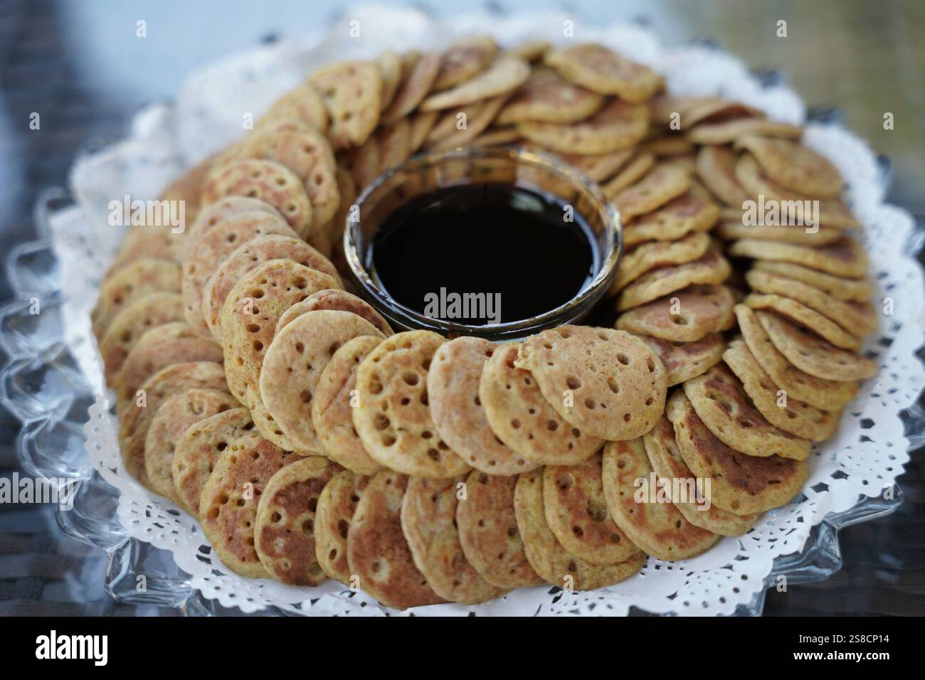 Eine wunderschön angeordnete Platte mit traditionellen Mini-Pfannkuchen serviert mit einer Schüssel mit reichem Dattelsirup. Perfekt für die Präsentation kultureller Küche, festliche tr Stockfoto