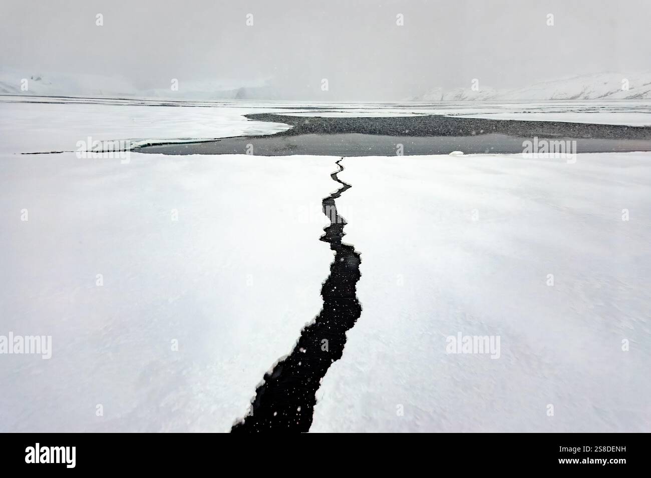 Im Eis Grönlands hat sich ein großer Riss entwickelt, der dunkles Wasser darunter freilegt. Die eisige Landschaft ist von Wolken bedeckt. Stockfoto
