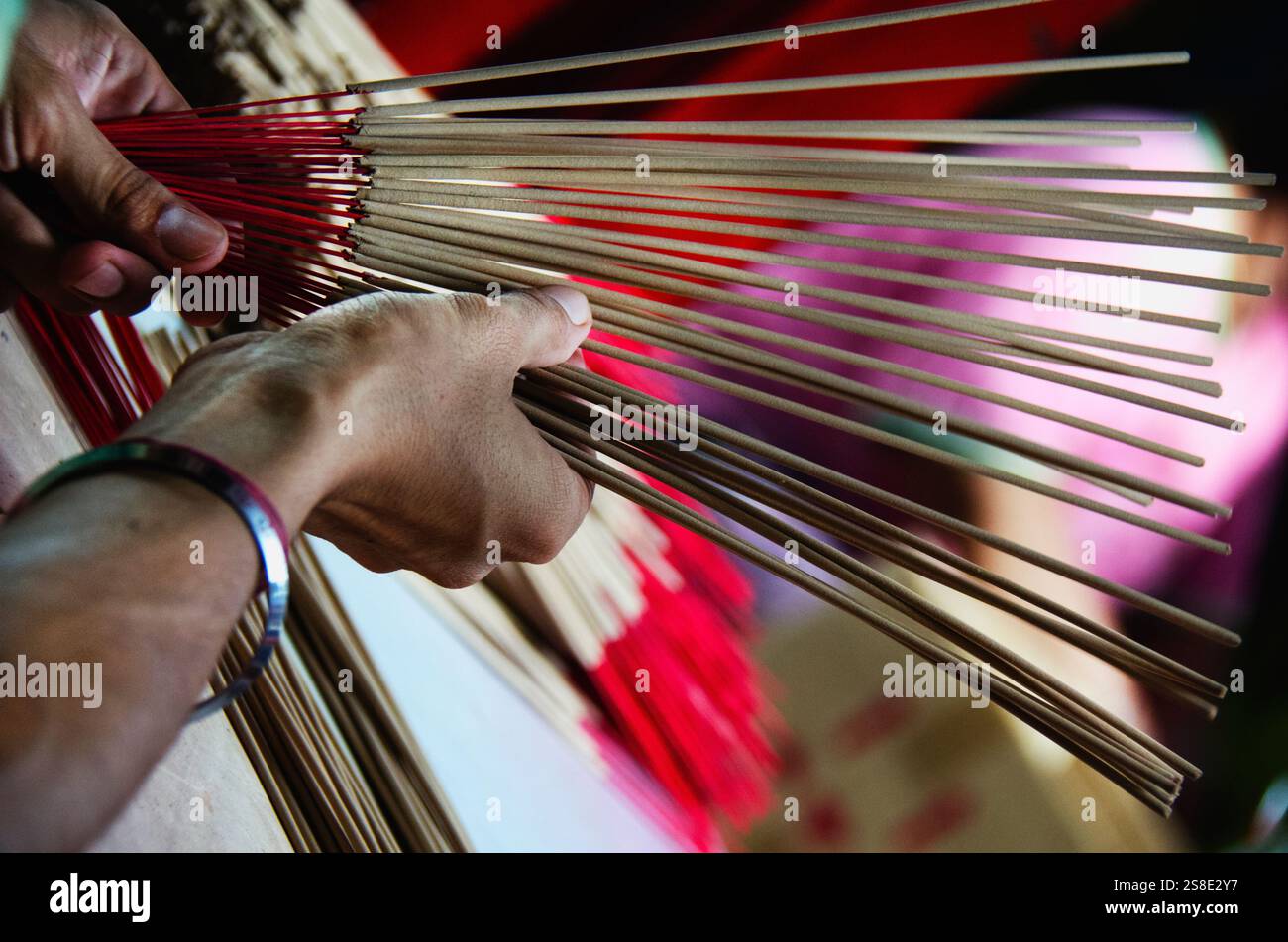 Nahaufnahme von Händen, die Räucherstäbchen mit roten Basen halten und arrangieren, die häufig in religiösen Ritualen und kulturellen Zeremonien in ganz Asien verwendet werden. Stockfoto