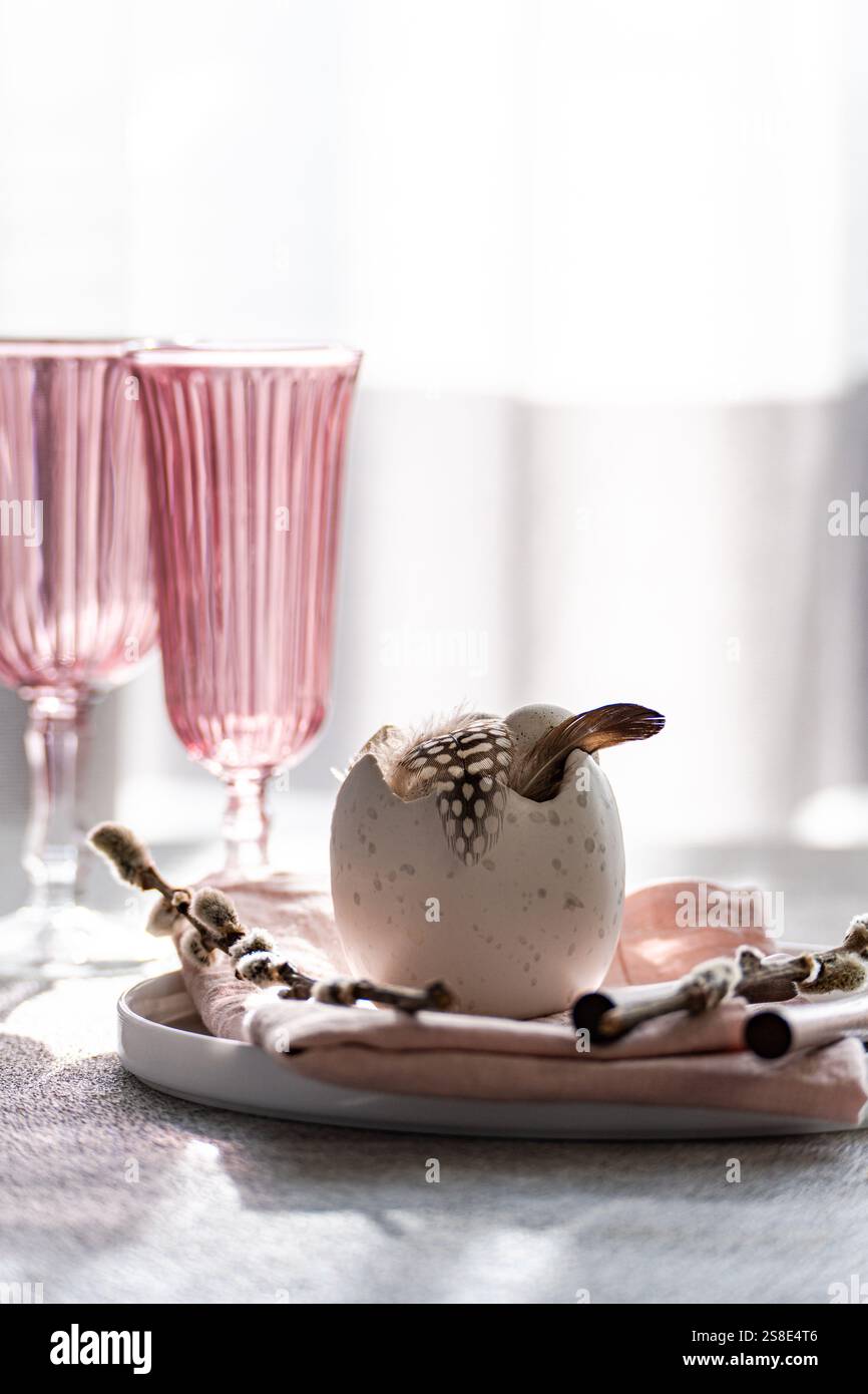 Stilvolles Osterrestaurant mit einem dekorativen Ei mit Federn, eingebettet auf einer pastellfarbenen Tischdecke, ergänzt durch ein elegantes rosafarbenes g Stockfoto