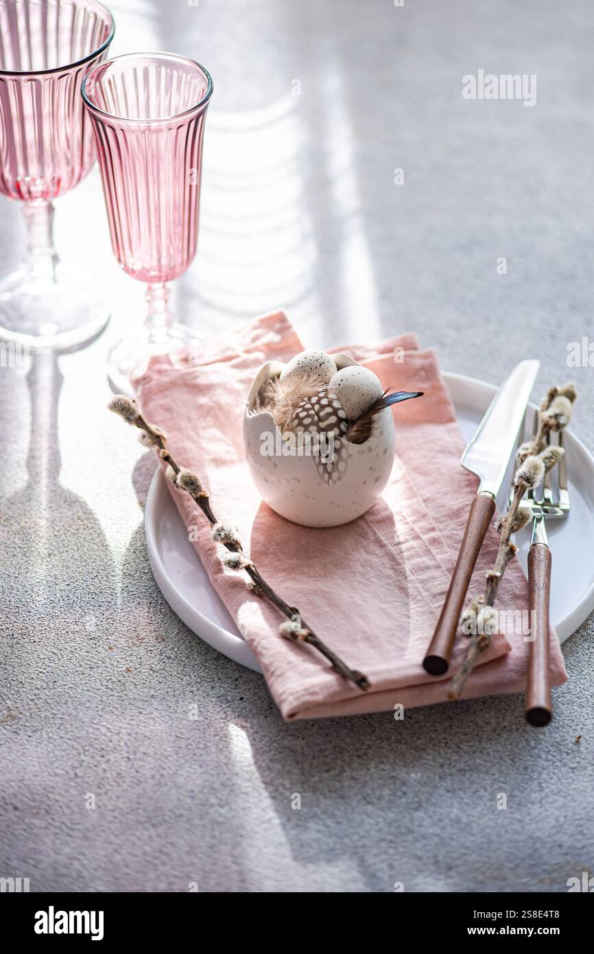 Ein eleganter und festlicher Ostertisch in sanften Pastelltönen. Der Fokus ist ein dekoratives Herzstück aus Eiern, umgeben von blühenden Weidenzweigen auf einem pi Stockfoto