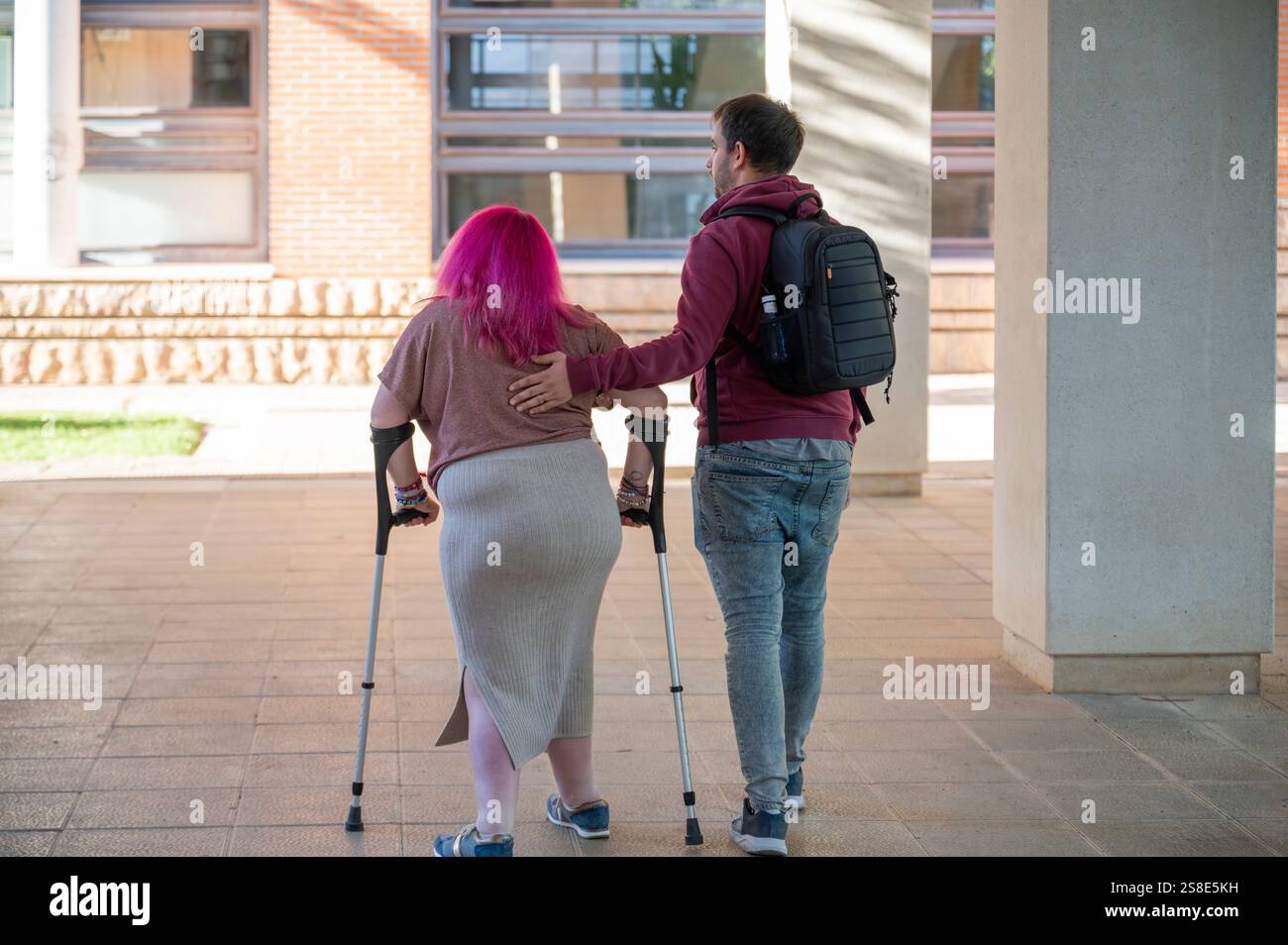 Ein unterstützendes Paar geht zusammen auf einem College Campus die Frau hat eine Behinderung durch Spina bifida. Ihre Verbindung wird hervorgehoben, einschließlich Stockfoto
