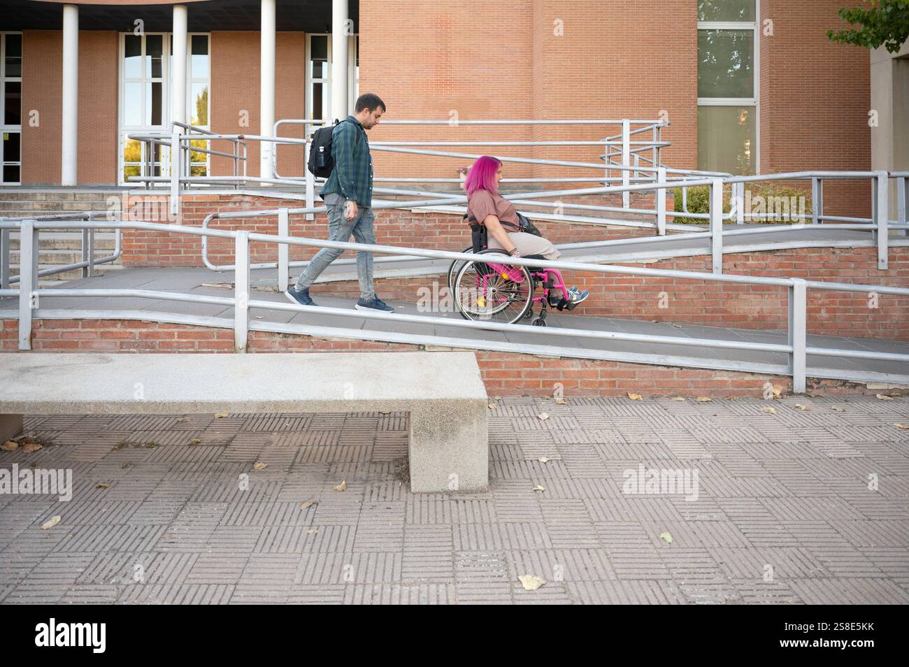 Junges Paar am College, das eine Frau im Rollstuhl aufgrund von Spina bifida zeigt, hebt das Bild die Zugänglichkeit und Inklusivität auf einem Campus mit Widder hervor Stockfoto